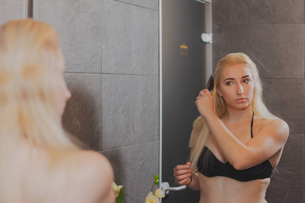 Красивая девушка стоит перед зеркалом и расчесывает волосы в купальнике в спа-центре
. - Фото, изображение