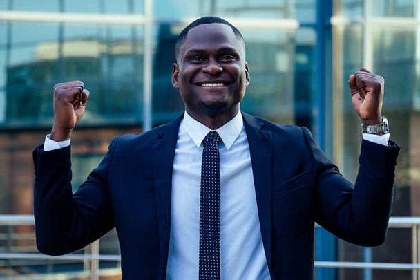 a handsome African American man in a black stylish suit and a white shirt rejoicing in success and thanking God against the background of city landscapes glass business centers. a good deal concept - Photo, Image