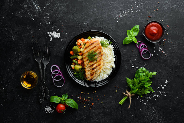 Baked chicken fillet with rice and vegetables on a black plate. Top view. Free copy space. - Foto, imagen