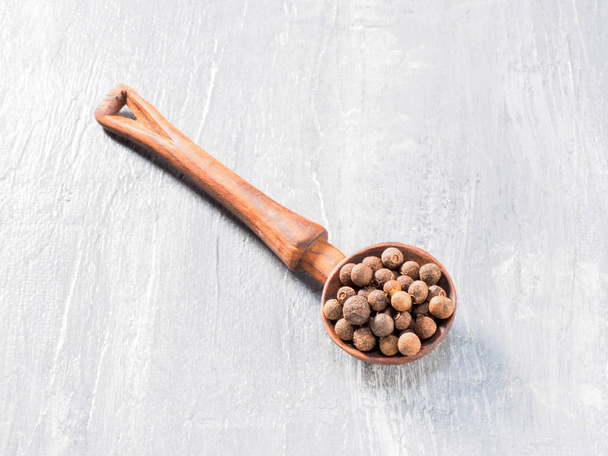 Allspice (Jamaica pepper) wooden spoon diagonally on grey cement - Fotografie, Obrázek