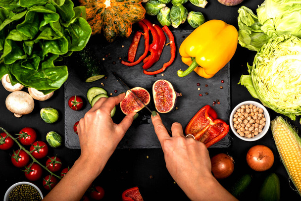 As mãos femininas cortam verduras em um fundo preto. Cozinhar comida vegetariana. Vista superior
. - Foto, Imagem