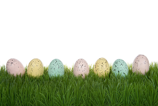 Reihe pastellfarbener Ostereier bespritzt mit Farbflecken, die isoliert auf einem weißen Hintergrund auf Gras liegen. - Foto, Bild