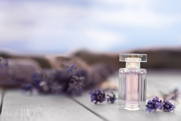 Flasche Luxus-Parfüm und Lavendelblüten auf weißem Holztisch im Freien. Raum für Text - Foto, Bild