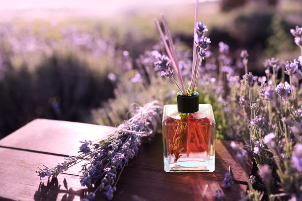 Reed air freshener with oil and fresh lavender flowers on wooden table in blooming field. Space for text - Photo, Image