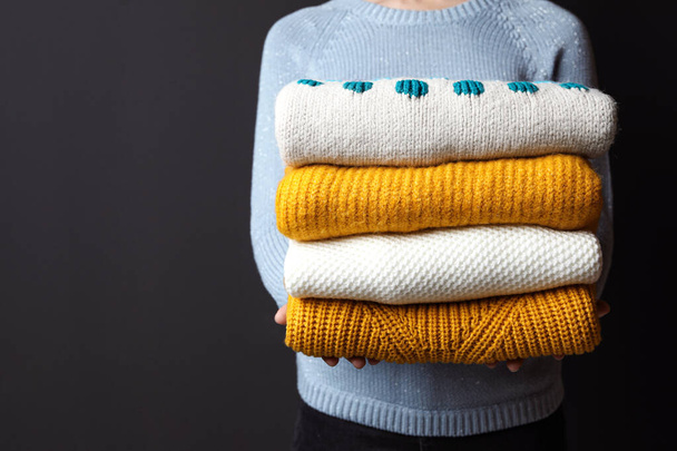 Woman holding pile of winter sweaters on dark background, closeup view. Space for text - Photo, image