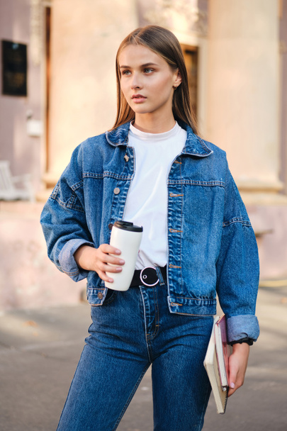 Молодая серьезная стильная студентка в джинсовой куртке задумчиво смотрит на улицу
 - Фото, изображение