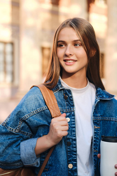 Giovane attraente ragazza studente casual in giacca di jeans felicemente guardando lontano in università all'aperto
 - Foto, immagini
