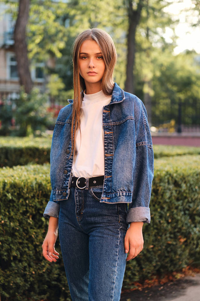 Bella ragazza dai capelli castani alla moda in giacca di jeans seriamente alla ricerca in macchina fotografica all'aperto
 - Foto, immagini