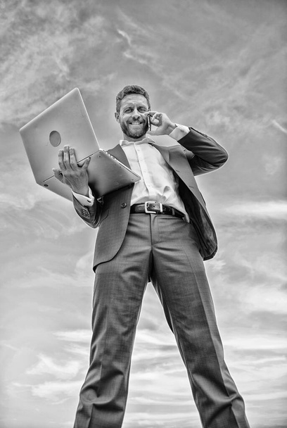 Guy formal suit modern technology manager entrepreneur answer phone call. Always in touch. Communicating skill. Man well groomed businessman holds laptop while speak phone blue sky background - Fotoğraf, Görsel