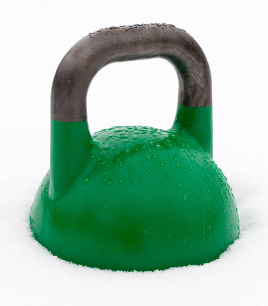 Kettlebell de entrenamiento de peso verde cubierto con gotas de agua afuera en la nieve
 - Foto, imagen