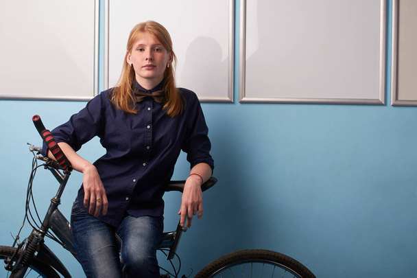Portrait of young woman riding bicycle against blue wall background - Фото, зображення