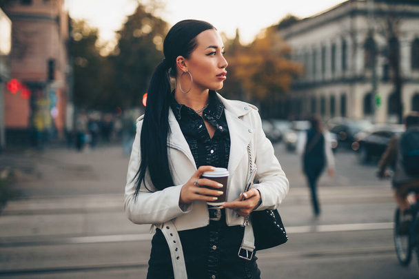 Beautiful woman holding paper coffee cup and enjoying to walk in the city - Фото, зображення