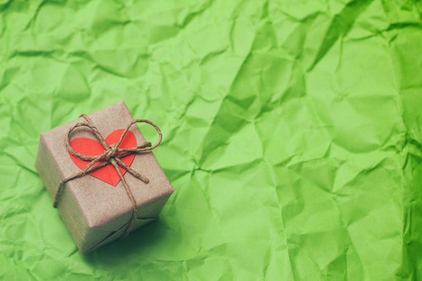 Gift box. Present wrapped in craft paper and tie hemp cord. Heart carton card. Green crumpled paper background. - Foto, Imagem