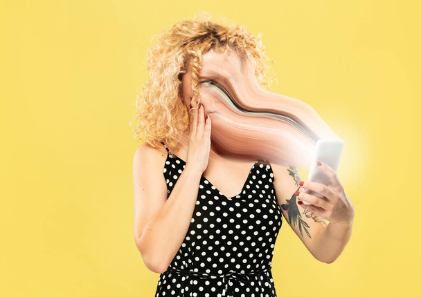 Young woman engaged by gadget and social media isolated on yellow background - Fotó, kép