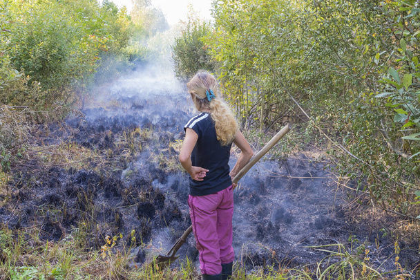Μια γυναίκα σβήνει μια φωτιά με ένα αγροτικό εργαλείο - Φωτογραφία, εικόνα