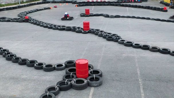 Unknown pilots competing in Karting Championship on a track made of old black car tires, aerial view. Media. Persons wearing protective uniform and helmet driving karts. - Photo, Image