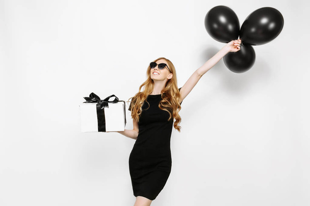 Happy elegant young girl in black dress happily holding gift wit - Photo, Image