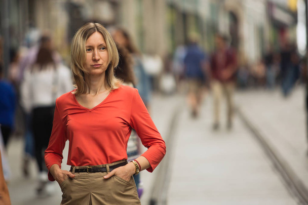 Blond woman in a red blouse standing on the street. - 写真・画像