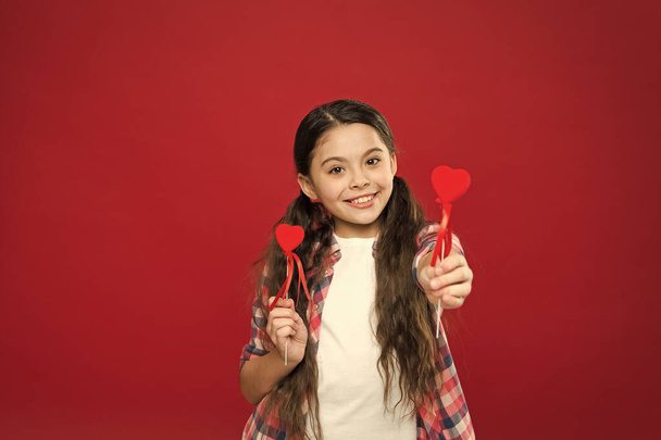 This is a day to say I love you. Small girl giving hearts on sticks. Cute girl with small red hearts. Small child with heart shaped decorations. Happy valentines day. The holiday of love and romance - Фото, изображение