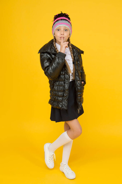 Keep secret. Fashion shop. Girl wear knitted hat and down jacket yellow background. Fashion concept. Warm clothing. Buy clothes for school season. Schoolgirl fashion outfit. Fall autumn winter - Foto, Imagen
