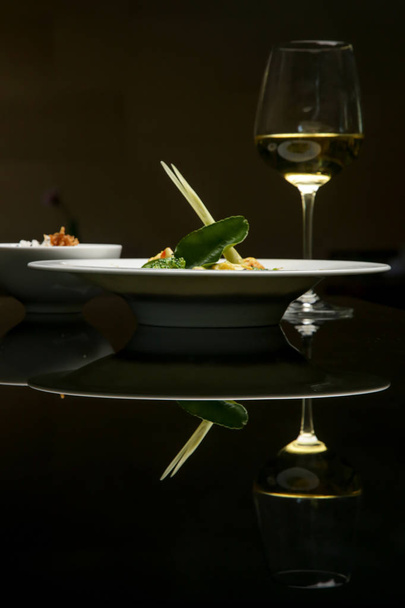 An exquisite minimalistic styled dish served in a bowl on black with reflexion. Creative restaurant meal concept. Haute couture food. Fine dining concept. - Photo, Image