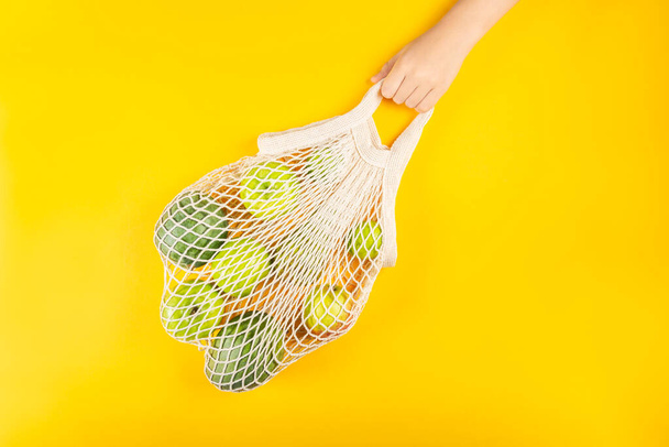 Kız elinde pamuk iplik, yeşil meyveli ağ torbası tutuyor. - Fotoğraf, Görsel