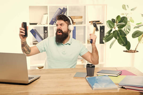 Most annoying thing about work in call center. Incoming call. Annoying client calling. Man bearded guy headphones office swing hammer on smartphone. Spoiled communication. Failed mobile negotiations - Fotoğraf, Görsel
