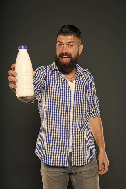 The best drink for your body. Bearded man holding bottle of milk drink on grey background. Happy hipster smiling with natural healthy dairy drink. Caucasian guy enjoying fresh yogurt drink - Foto, imagen