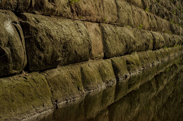 Antigua muralla de piedra cuya base está inundada de agua
 - Foto, Imagen