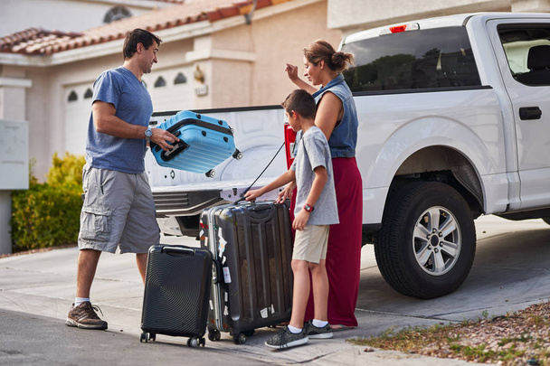 hispanic family packing luggage into pickup truck in front of house - Фото, изображение