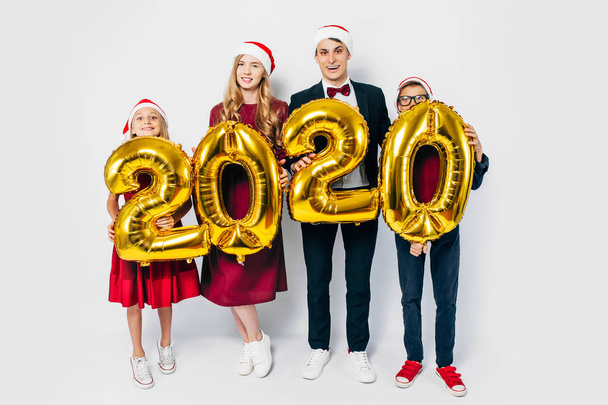 Young happy family with kids wearing Santa hats holding balloons - Foto, afbeelding