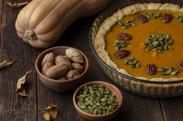 homemade pumpkin pie , pumpkin seeds and autumn leaves on a wooden background - Photo, Image