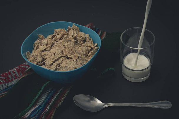 Cereal con leche y platanos sobre un mantel, con una cuchara y un vaso en fondo negro - Foto, Imagem