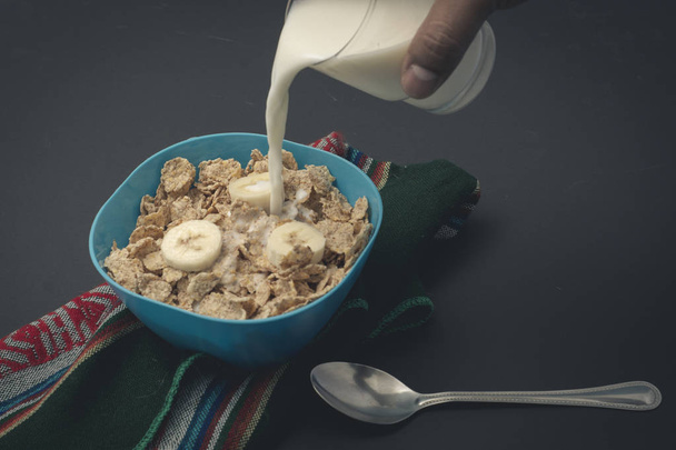 Cereal con leche y platanos sobore un mantel, con una cuchara y un vaso en fondo negro. - 写真・画像