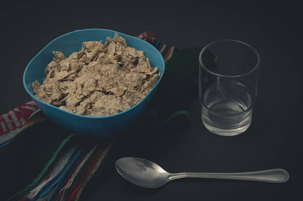 Cereal integral en plato azul sobre mantel con vaso y cuchara - Foto, Imagem