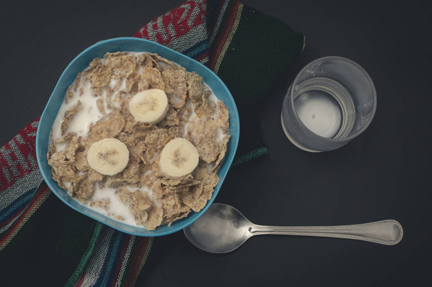 Cereal con leche y platanosrae un mantel, con una cuchara y un vaso en Wago
 - Фото, зображення