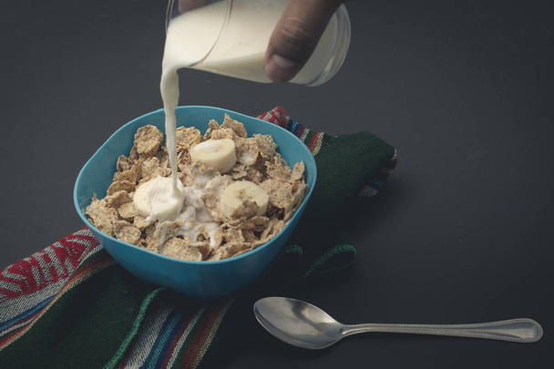 Cereal con leche y platanos sobre un mantel, con una cuchara y un vaso en fondo negro - Fotografie, Obrázek