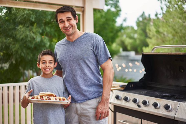 proud father and son showing tray of grilled hot dogs - Фото, изображение