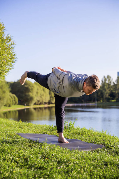 Inspired man doing yoga asanas in city park. Fitness outdoors and life balance concept. - Fotó, kép