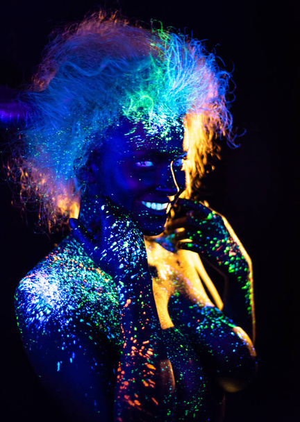 Body art and contact lenses glowing in ultraviolet light. Woman smiling, painted in fluorescent powder. Stars in the eyes - Foto, afbeelding