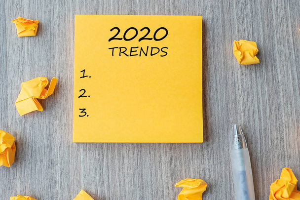 Trendwort 2020 auf gelbem Zettel mit Stift und zerbröseltem Papier auf weißem Papier - Foto, Bild