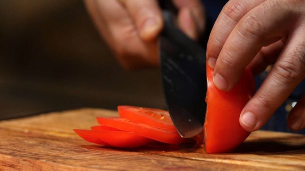 rote Tomaten auf Holzbrett schneiden. Archivmaterial. Koch schneidet Tomaten auf einem Holzbrett - Foto, Bild