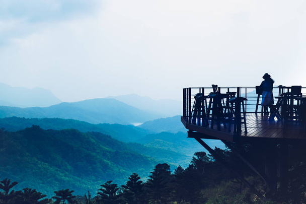 Жінка мандрівник стоїть за межами кафе тераси на вершині пагорба і п'є каву з красивим видом на гори
. - Фото, зображення