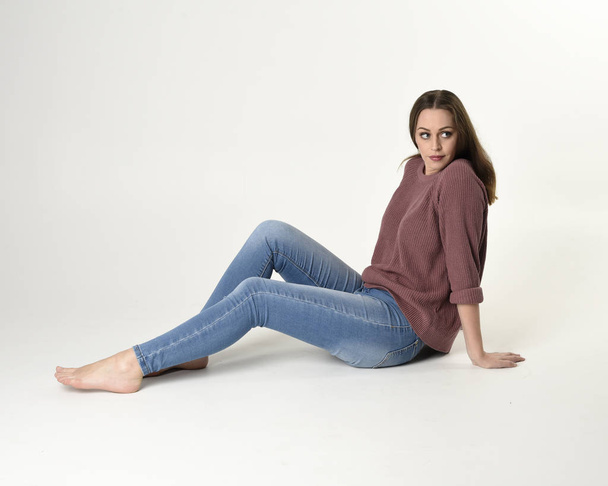 portrait complet de femme brune portant un jean et un pull rose. pose assise avec un fond de studio blanc
. - Photo, image