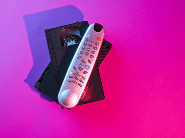 Retro wave style tv remote and  video cassette with neon pink-blue light. 80s. Top view - Photo, Image