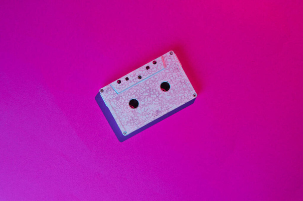 Retro wave style audio cassette with neon pink-violet light. 80s. Top view - Foto, Imagen