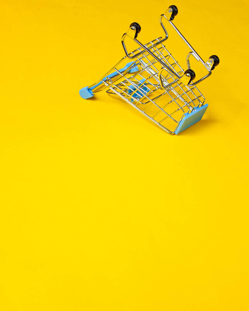 Minimalist shopping concept. Empty inverted miniature shopping trolley on yellow background. Copy space - Foto, imagen