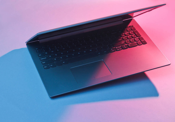 Modern laptop with vibrant gradient pink  blue holographic color lights. Minimal office surrealism concept. - Photo, Image