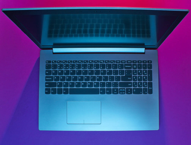 moderner Laptop mit lebendigem Gradienten rosa-blauen Neonlichtern. Minimalismus. Ansicht von oben - Foto, Bild