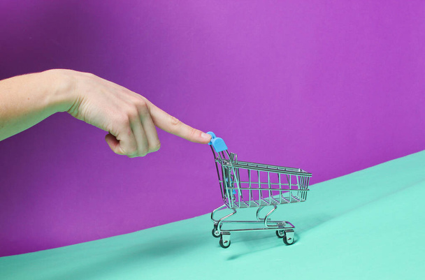 Dedo femenino empuja hacia arriba pendiente vacío mini carrito de compras. Concepto de compra, entrega - Foto, Imagen